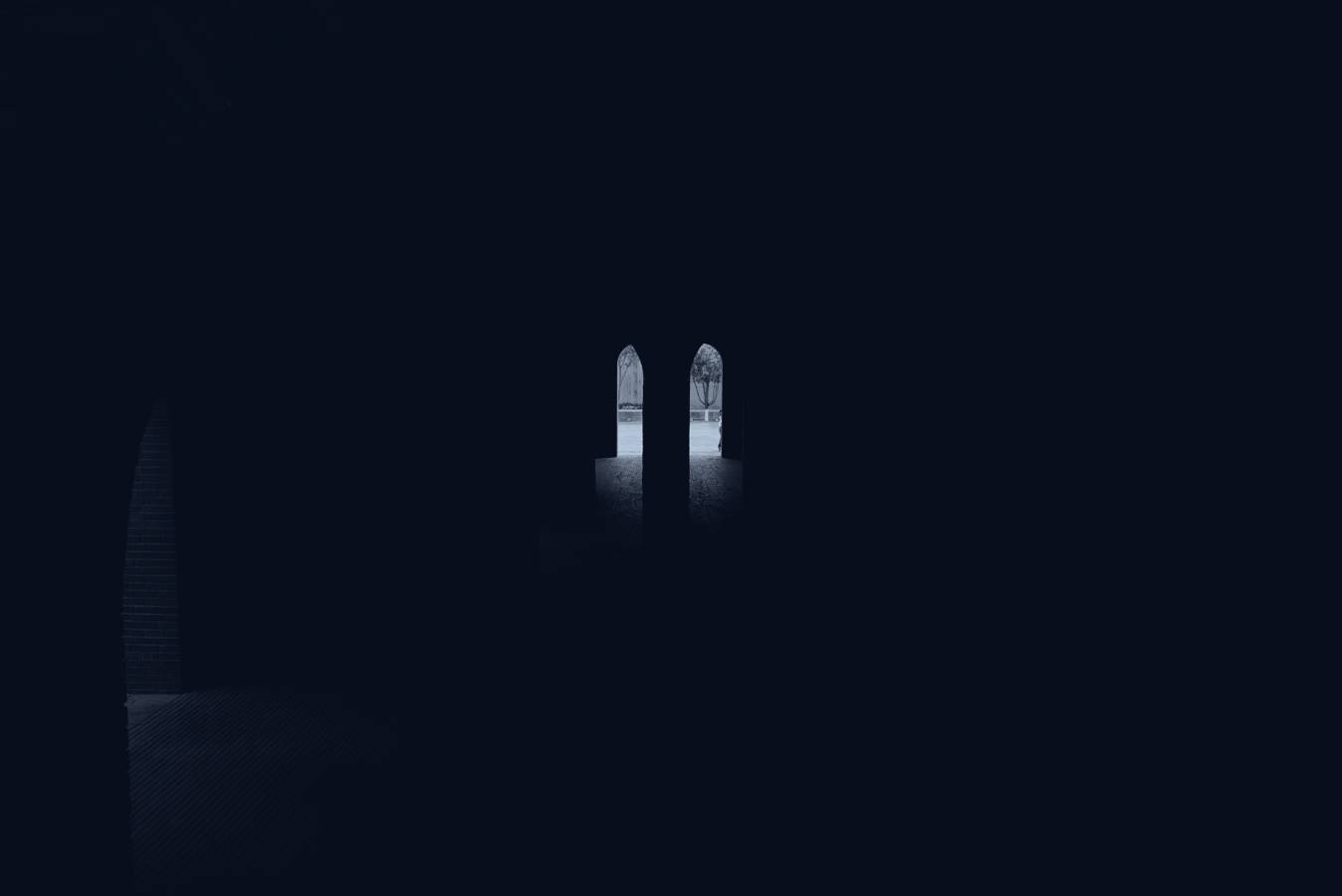 A dark interior of arched doorways with light beyond